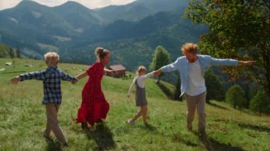 Positive parents playing outdoor games with carefree children on green sunny hill. Playful family having fun together enjoy summer holiday in mountains. Happy couple with kids fooling on nature.