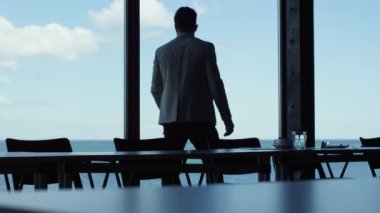 Confident businessman walking browsing tablet at ocean view hotel. Good looking man holding device in panoramic window dark office. Ceo professional silhouette working on pad. Business concept