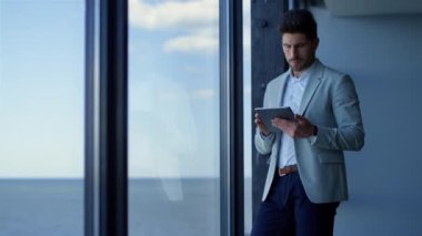 Happy businessman using tablet computer in ocean view office. Ceo professional reading good news in online app pad. Successful entrepreneur looking panoramic window. Corporate worker lifestyle 