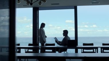 Manager silhouette talking executive at panorama window place. Unrecognized finance analyst ceo checking reading report papers at secretary dark room. Anonymous subordinate assisting boss in office 