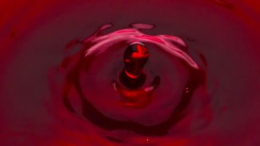 Daire şeklinde şarap damlaları cam kapaklara düşüyor. Alkolik damlacık kırmızı sıvıya sıçrıyor. Terbiyesiz kütle, yumak yüzeyinde dalgalanmalar yaratıyor. Akan içecek dalgaları yavaş çekimde 