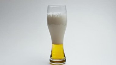 Zıpzıp, filtresiz, köpüklü, süper yavaş çekim. Köpüklü alkollü içecek, temiz cam kapağı. Kadehlerin beyaz arka planında kaynayan taze gemi sıvısı. Serinletici soğuk bira birası