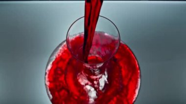 Kapalı mekandan kırmızı şarap kadehi dökülüyor. Alkolik sıvı sürahi süper yavaş çekimde. Şeffaf cam serpiştiren sersemletici gül makrosu. Merlot dalgası saf konteynırın içinde