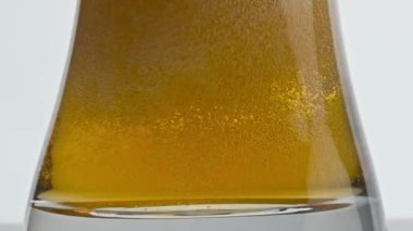 Buzlu bira cam dipte fokurduyor. Şeffaf kadehte ağır çekimde zıpzıp alkolik sıvısı akıyor. Pastörize arpa birası kaynayan kabın beyaz arka planı. Sarhoş edici bir içecek.