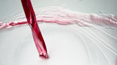 Sarhoş edici kırmızı içecek kadehi ağır çekimde doldurur. Alkollü sıvı temiz şarap kadehi beyaz arka plan dökülüyor. Şarap, cam üst görüntüde dalgalar oluşturur. Gül rengi jet hızla su sıçratıyor şeffaf camlar