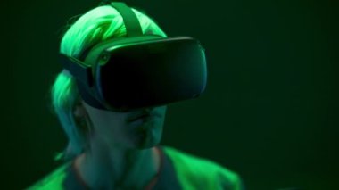 Focused man watching VR headset in neon light closeup. Blonde gamer looking goggles playing videogame over dark multi coloured background. Guy enjoying 3d movie. Future, gadgets, technology concept 