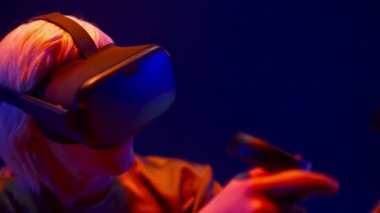 VR headset guy playing in neon light. Closeup involved man using futuristic technology helmet for simulation 3D videogame. Male person virtual reality goggles experiencing augmented adventure 