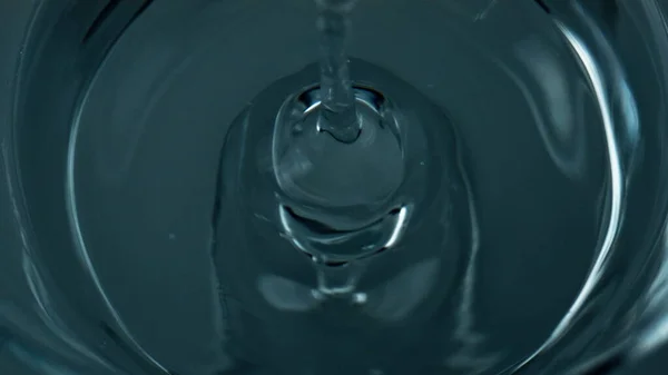 Liquid droplet falling water top view. Closeup refreshing drink waving rippling in transparent cup. Pure refreshing drop splashing smooth surface on glass jug beverage. Wellness moisturizing concept.