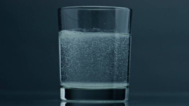 Air bubbles rising glass surface closeup. Acid fluid in transparent cup at dark background. Dissolved tablet painkiller bubbling in pure mineral water. Quenching thirst refreshing beverage concept.