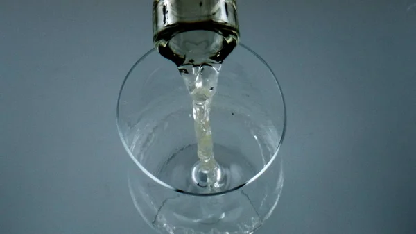 Bottle filling wine glass closeup. Top view cool alcohol beverage pouring goblet. White liquor sauvignon splashing bubbling in transparent cup. Celebrating anniversary evening with grape fizzy drink.