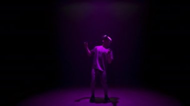 Neon man experiencing virtual reality in dark cyberspace. Focused player explore online simulation in ar headset. Unrecognized gamer enjoying metaverse holding controllers. Teenager lifestyle concept