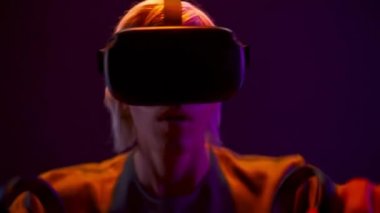 Active vr glasses man playing online game with joysticks closeup. Energetic gamer enjoying virtual reality with controllers. Blonde guy using gamepad for quest adventure videogame at neon light