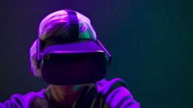 VR glasses person dancing metaverse closeup. Esport blonde gamer using new technology goggles playing game neon light background. Millennial man relaxing with 3d headset. Cyberspace and future concept