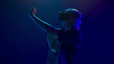 Involved guy visit virtual party closeup. Modern man immersed in abstract neon vr world. Young person augmented reality headset dancing alone slow motion. Metaverse technology future concept