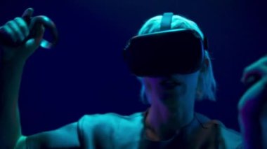 Scared man playing handheld trackpads videogame closeup. Nervous gamer using gadget for virtual reality on neon background. Futuristic goggles youngster testing horror game. Future technology concept 