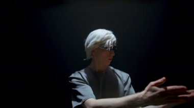 Gamer explore virtual reality in dark room. Focused man swiping select objects on invisible panel. Futuristic player experiencing console simulation in ar goggles. Hi tech metaverse entertainment.
