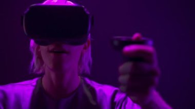 Energetic gamer playing online videogame with gamepads closeup. Active vr glasses man enjoying virtual reality with controllers. Blonde guy using joysticks for quest adventure game at neon light