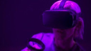 Closeup excited man experiencing VR headset videogame. Impressed gamer using gadget for virtual reality on neon background. Male in futuristic goggles playing controllers. Future technology concept 