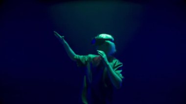 Sanal gerçeklik oyuncusu neon ışıklarla oynuyor. Görünmez nesnelere dokunarak simülasyonu keşfeden sarışın adam. Tanınmayan sarışın ergen metaverse oyunu yaşıyor. Moda haftasonu eğlencesi.