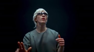 Hayret verici VR oyuncusu metaverse simülasyonunu yakından oynuyor. Gelecekçi adam dijital gözlüklerle artırılmış gerçekliği keşfediyor. Gelecekçi sarışın adam karanlık siber uzayda hareketler yapıyor. Heyecanlı siber oyuncu.