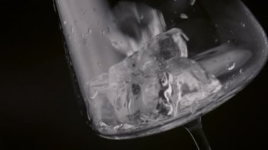 Temiz buz küpleri siyah arkaplanda boş şarap bardağına dökülüyor. Donmuş bloklar şeffaf temiz kadehe süper yavaş çekimde fırlatılıyor. Canlandırıcı içecek hazırlamak için gerekli malzemeler.