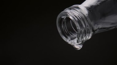 Şişeden damlayan son damlalar çok yavaş çekimde yakından geliyor. Siyah arka planda cam şişeden düşen temiz su damlaları. Sağlıklı yaşam tarzı kavramı için taze saf su.