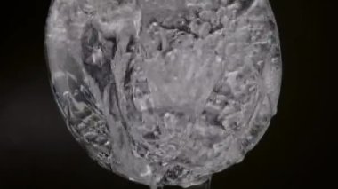 Temiz su, siyah arka planda şeffaf şarap kadehlerine dökülüyor. Dopdolu bardaktan fırlayan dönen bir içecek. Hava kabarcıkları temiz kadehlerin içinde daireler çiziyor. Soğuk içecek..