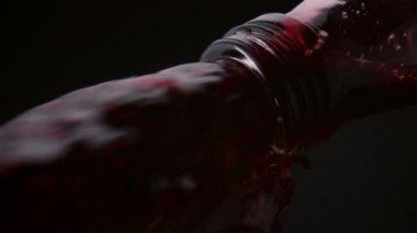 Şişe boyundan dökülen kırmızı şarap akıntısı yakından geliyor. Siyah arka plandaki cam konteynırdan taze alkol sızıyor. Lezzetli Merlot 'un fırtınalı jeti Süper yavaş çekimde düşüyor.