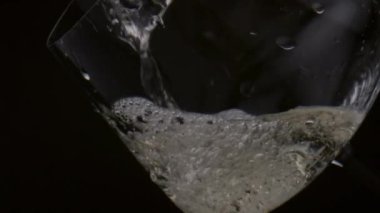 Akarsu gurme beyaz şarap siyah arka planda zarif şarap kadehine akıyor. Altın alkol, şeffaf kadehin içinde köpüren köpükler çıkarıyor. Lezzetli Chardonnay 'i ağır çekimde dolduruyorum..