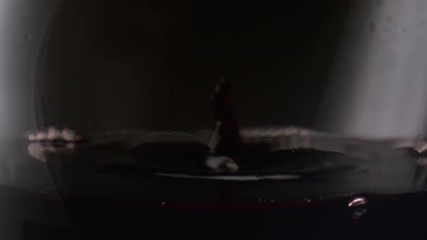 滴落水晶般的酒杯 红葡萄酒在黑色背景的近处 葡萄饮料中的液滴在玻璃杯中荡漾着光滑的液体表面 Merlot在透明杯子里挥动着 动作非常慢 — 图库视频影像