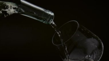 Büyüleyici bir manzara, şişeden temiz bardağa altın şarap dökme görüntüsü, yakın plan. Akım sarı alkol içeceği süper yavaş çekimde şarap bardağına akıyor. Gurme içecek konsepti.