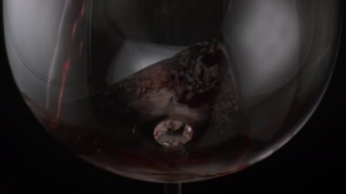 Kırmızı şarabı şeffaf cam bardağa doldururken çok yavaş çekimde. Siyah arka planda kristal şarap kadehini dolduran kırmızı şarap içeceği. Şişeden akan üzüm suyu..