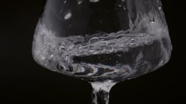 在黑色的背景上 一股湍急的淡水注入杯中 近在咫尺 透明的透明液体在水晶玻璃内旋转 纯气泡在玻璃窗中流动 健康饮料概念 — 图库视频影像