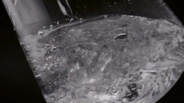 Buzlu bardağa taze su dökerek. Kristal sıvı şeffaf bardağı ağır çekimde dolduruyor. Saf temiz mineral içeceği. Siyah arka planda köpükler fışkırıyor..