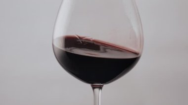 Kristal şarap kadehinde leziz bir Merlot dalgası var. Şeffaf kadehin içinde süper yavaş çekimde dönen muhteşem kırmızı alkol içeceği. Beyaz arka planda parti için gurme burgundy sıvısı.