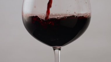Burgonya şarabı kadehini çok yavaş çekimde dolduruyor. Şeffaf şarap kadehinde akan gurme kırmızı alkol köpükler yapıyor. Beyaz arkaplanda kristal bulaşık takımı dolduruluyor