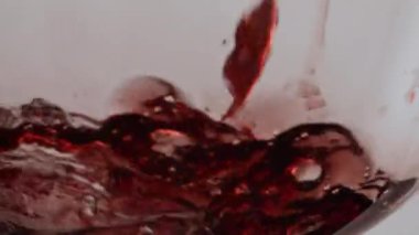 Kapalı kırmızı şarap akıntısı boş kristal kadehi süper yavaş çekimde dolduruyor. Beyaz arka planda şeffaf şarap kadehinin içine dökülen Burgundy alkollü içecek. Parti için güzel bir içki..