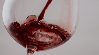Cam kadehte kırmızı lezzetli şarap dökülüyor. Şeffaf şarap kadehi döken gurme cabernet beyaz arka planda su sıçratıyor. Ağır çekimde akan bordo alkollü içecek..