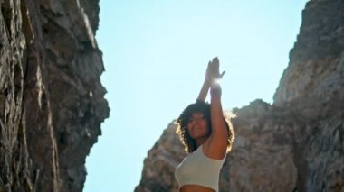 Elleri havada, açık havada parlak güneş ışığında duran zinde bir kadın. Rahatlamış bir kız Ursa sahilinde yaz sabahı yoga yapıyor. Yüksek kayalık deniz kıyısında spor yapan zayıf bir kadın..