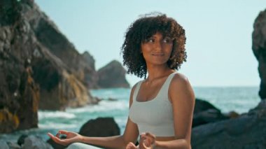 Afrika kökenli Amerikalı kız Lotus pozisyonunda meditasyon yapıyor. Güzel manzaralı kayalık bir sahile benziyor. Çekici bir genç kadın Ursa sahilinde oturuyor. Rahatlamış kıvırcık bayan doğayla barışın tadını çıkar..