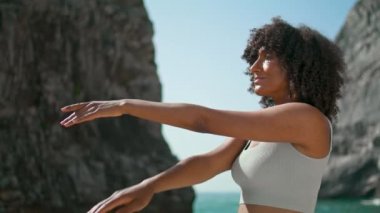 Huzurlu bir yogi kızı Ursa sahilinde esneme egzersizleri yaparak el ele tutuşuyor. Gülümseyen Afro-Amerikan sporcu kadın dışarıda yoga yapıyor. Sağlıklı vücut için kadın eğitimi.