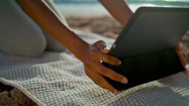 Bilinmeyen kız plajda tablet kullanıyor. Yakın çekim. Genç Afro-Amerikalı kadın yoga minderinin üzerine sekme bilgisayarı koyuyor açık hava eğitimine hazırlanıyor. Sıska bayanın doğada çalışmak için modern bir aleti var..