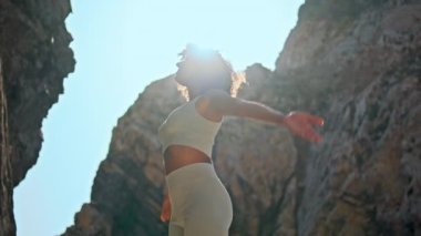 Huzurlu genç bir kadın namaste 'nin ellerini önünde tutuyor gülümseyen kamerayı yakından çekiyor. Spor giyimli mutlu sakin kız parlak güneş ışığı altında duruyor kayalık Ursa plajında. Kıvırcık kadın meditasyonu