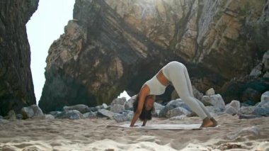 Esnek Afro-Amerikan kadın, köpeğe doğru eğilip Ursa kumsalında yoga yapıyor. Bir bacağını kaldıran genç ve güçlü bir kız güneşli bir günde güneş selamı veriyor..