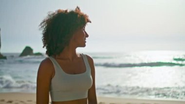 Rahat bir Afrikalı Amerikalı kadın güneş doğarken deniz manzarasına bakıyor. Sahilde durup yaz akşamının tadını çıkaran tasasız mutlu kız. Huzurlu bayan doğada huzur ve uyumu sağlıyor..