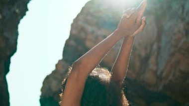 Bilinmeyen kıvırcık esmer kız dışarıda, parlak güneş ışığı altında ayakta duran savaşçı pozu veriyor. Genç sportif kadın güneşli gökyüzüne el kaldırarak Rocky Beach Ursa 'da yoga yapıyor. Refah kavramı.