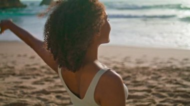 Kum plajında boynunu uzatan Afrikalı Amerikalı kız. Rahatlamış, kaygısız bir kadın, gün doğumunda elleriyle başını tutup spor yapıyor. Zayıf sporcu kadın antrenmandan önce ısınıyor.