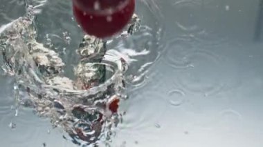 Yakın plan domatesler sıvıyı yakından sıçratıyor. Lezzetli organik gıda reklamı. Kırmızı taze sebzeler şeffaf suyla yıkanır. Olgun renkli bahçe hasadı. Sağlıklı zindelik besin.