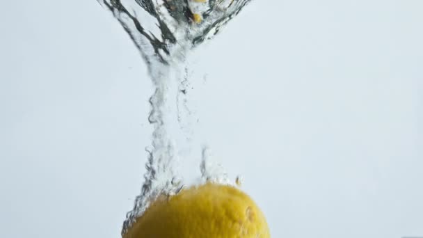 淡い背景に新鮮なレモン滴下水を閉じます 有機熱帯果実が泡状の液体に浮かんで落ちます さわやかなレモネード成分が渦巻くバウンス 黄色の夏のインスピレーションの概念 — ストック動画