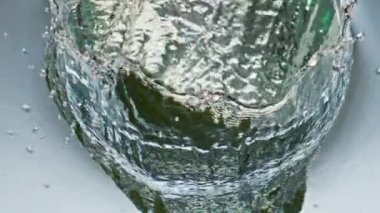 Yakından taze avokado, pürüzsüz su yüzeyine sıçrıyor. Sağlıklı organik bileşen, saydam sıvıya dönüşüyor. Egzotik yeşil meyve, cam kapları düşürüyor. Doğal detoks gevşeme kavramı.